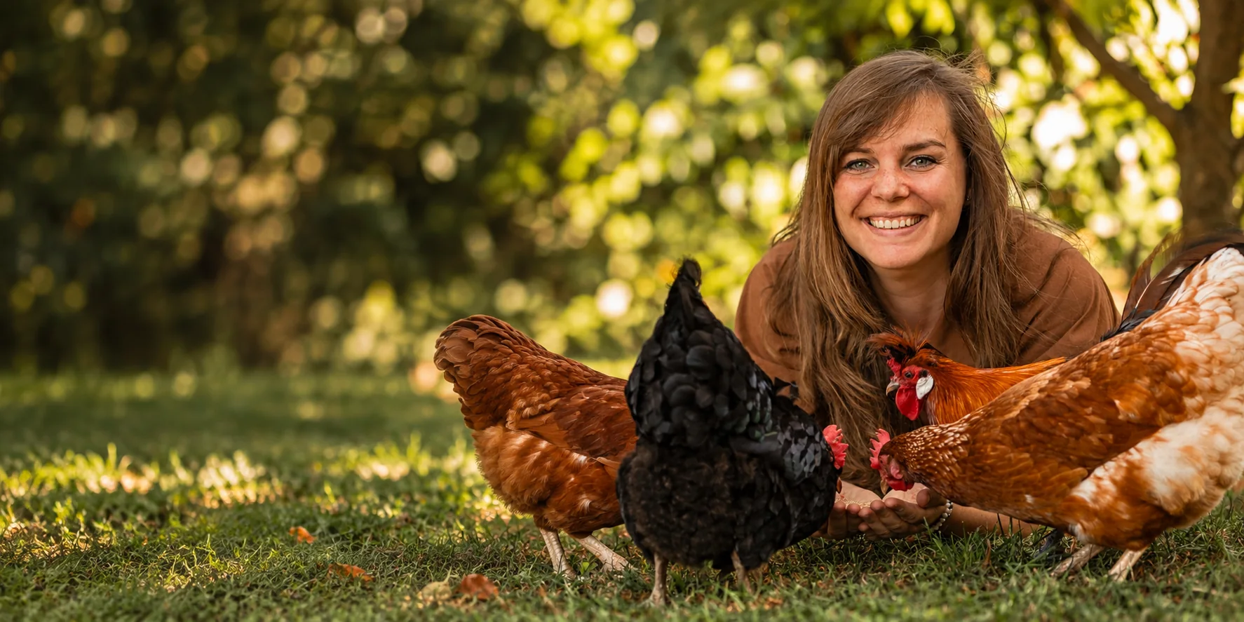Ramona liegt lächelnd im Gras, umgeben von drei Hühnern